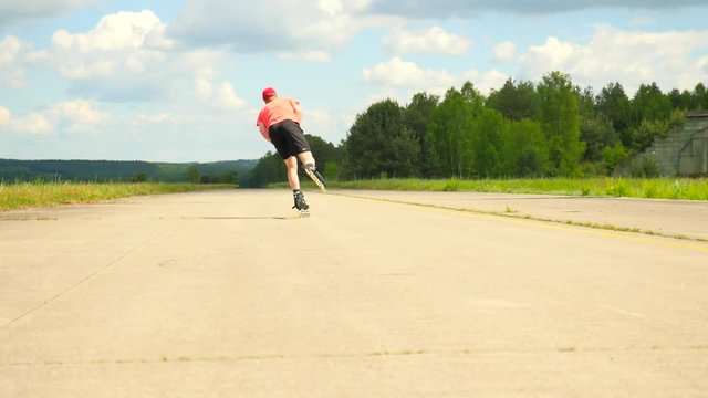 Rear view to inline skater in green running singlet . Outdoor inline skating on smooth asphalt in sunny summer day. Light skin man on the road, moving with center of gravity.
