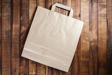 Fototapeta premium Recycled craft paper shopping bag on vintage wooden table background. Top view.