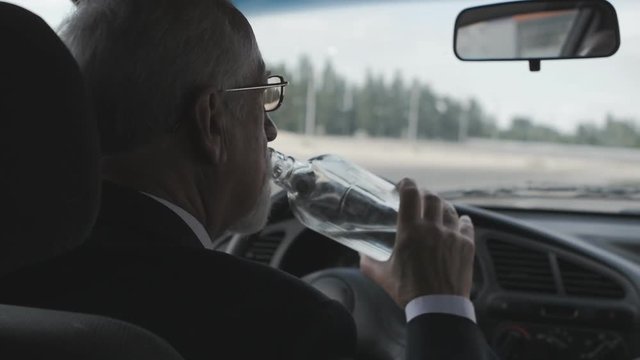 Senior man drinks vodka while sitting in the car. Drunk Driver.