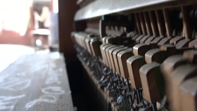 CLOSE UP DOF: Old obsolete dusty piano from the inside. Hammers striking strings tuned to produce the note when a piano key is pressed. Dusty vertical piano playing music in old abandoned ruined house