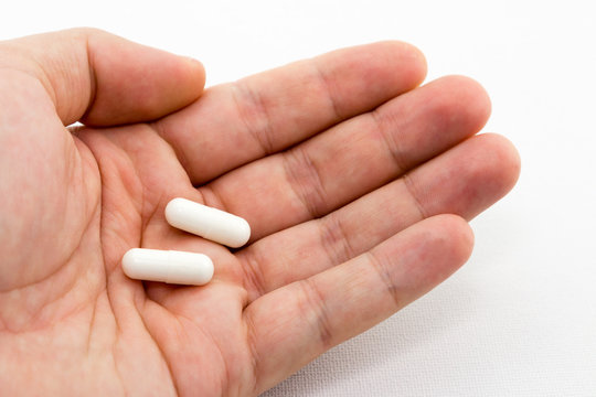 A human hand holding two white pills. This image can be used to represent medication or a doctor's prescription.