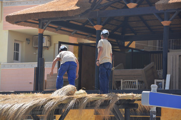 obreros reparando un tejado de paja