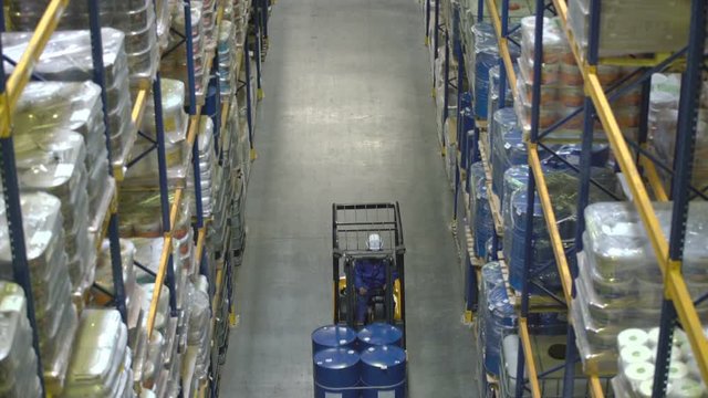 Warehouse worker on forklift transporting barrels with chemical substance
