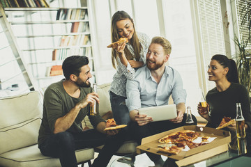 Young people eating pizza, drinking cider and watching tablet in the room
