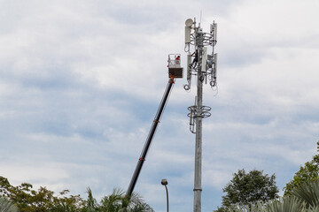 Two workers on crane installing mobile network telecommunication antenna