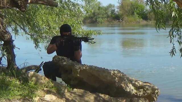 A Russian special forces soldier in a balaclava hides behind a stone and aims from a crossbow. Marine recon.