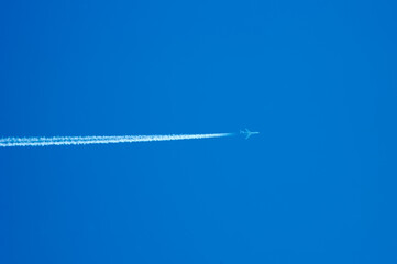 Passenger jet flying high in clear blue sky, leaving long white trail