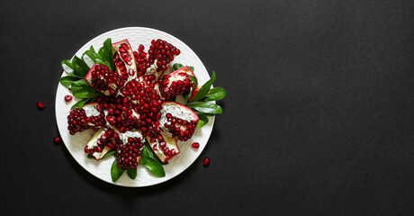 On white plate a ripe broken pomegranate fruit isolated on a black background, copy space.