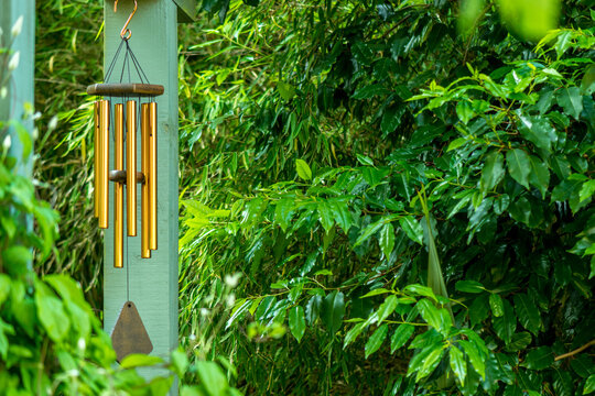 Brass Tubular Style Wind Chimes Hanging From Pergola In Garden