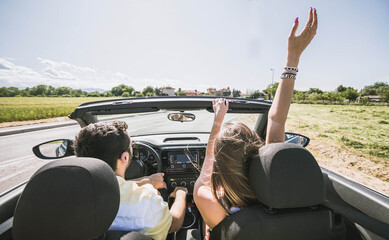 Traveller happy couple driving on the road into in a sports car rasing their arms to the sky