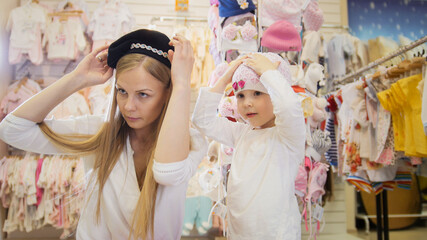 Mother and daughter try on cute beanies in front of the mirror