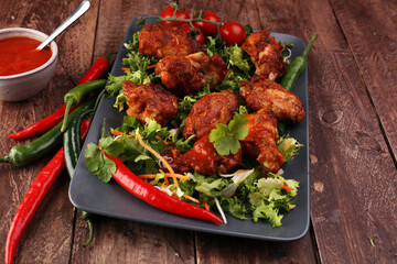 barbecue chicken wings close up on wooden tray with red spice sauce and salad