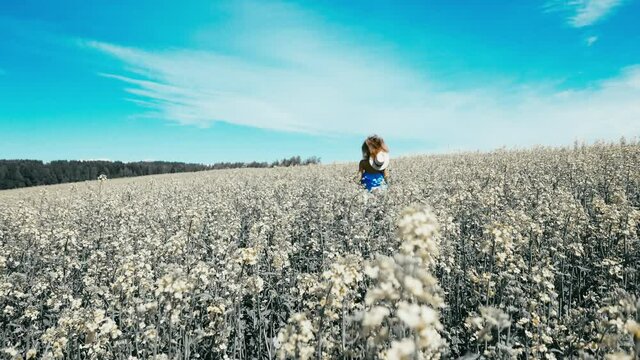 Attractive Caucasian female wearing blue dress and straw hat standing in a rapeseed field. Turning and running away from camera. 60 FPS SLOW MOTION, 4K UHD RAW edited footage