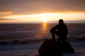 Obraz na płótnie Canvas Man on rock on the sea in the ice - silhouette