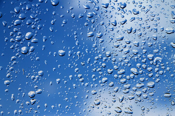 Rain drops on window with blue cloudy sky in background , spring rainy day 