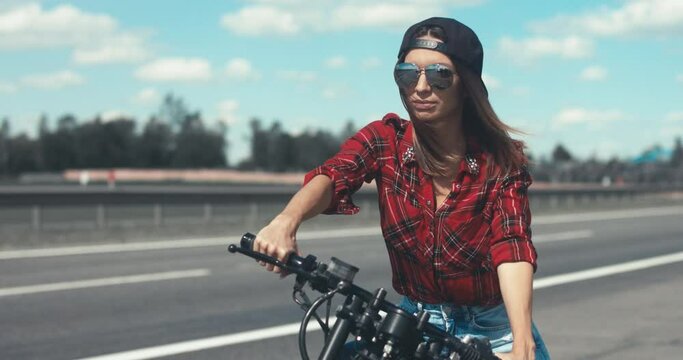CINEMAGRAPH - seamless loop. Young Caucasian girl with brown hair sits on a motorbike near a road. 4K UHD RAW edited footage