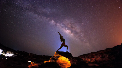 Landscape with Milky way galaxy. Night sky with stars and silhouette woman practicing yoga on the...