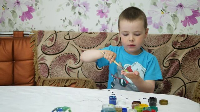 The boy draws paints in the house at the table.