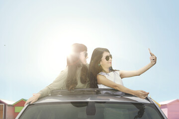 Young women taking selfie photo on car sunroof