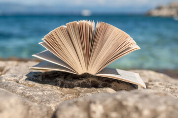 Open book at beach near the sea during bright sunny summer holiday vacation day  