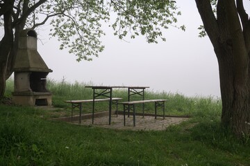 Table, bench and fireplace between trees during misty morning. Slovakia