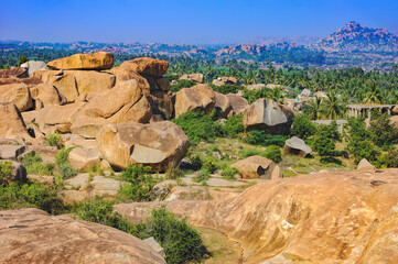 Landscape with unique mountain formation with amazing stones, palm trees and bushes in Hampi, India