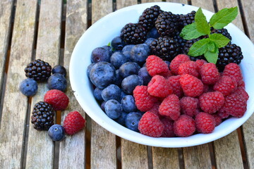 Raspberries, blackberries and blueberries in a bowl on a wooden table