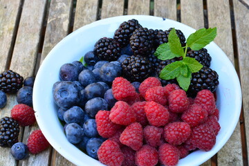 Raspberries, blackberries and blueberries in a bowl on a wooden table