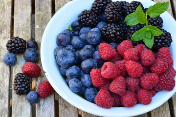 Raspberries, blackberries and blueberries in a bowl on a wooden table