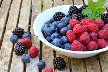 Raspberries, blackberries and blueberries in a bowl on a wooden table