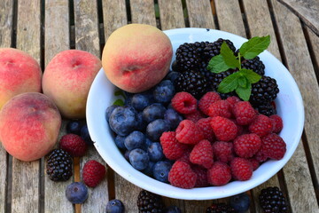 Raspberries, blackberries and blueberries with peaches in a bowl on a wooden table