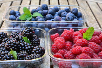 Raspberries, blackberries and blueberries in a plastic box on a wooden table