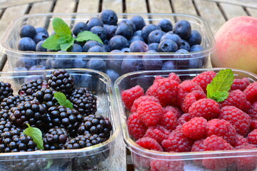 Raspberries, blackberries and blueberries with a peach in a plastic box on a wooden table