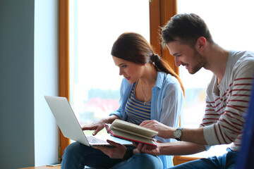 Fototapeta premium Happy young couple sitting on the windowsill, use a laptop at home