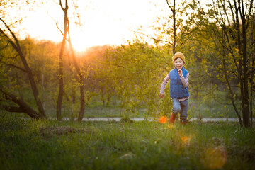 Portrait of smiling kid boy running in the park on sunset. Happy child walking outdoors on a sunny day. Lifestyle.