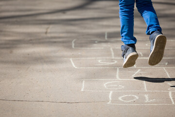 Closeup of boy's legs and hopscotch drawn on asphalt. Child playing hopscotch on playground outdoors on a sunny day. outdoor activities for children.