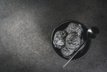Trendy food. Black ice cream with black sesame, in a black bowl on a black stone table, with a spoon. Copy space top view