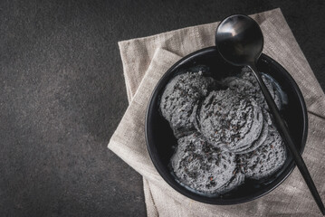 Trendy food. Black ice cream with black sesame, in a black bowl on a black stone table, with a spoon. Copy space