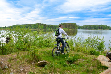 Naklejka premium Biker with a mountain bike on the shore of a beautiful lake covered with greenery