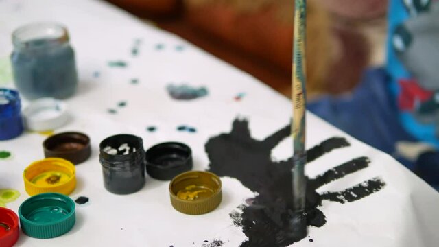 The boy draws paints in the house at the table.