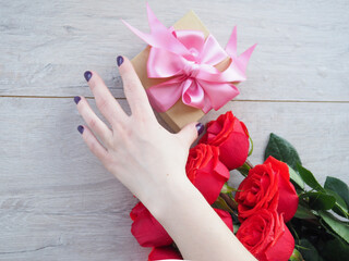 Fototapeta na wymiar Gift box on woman hands and bouquet of beautiful roses.
