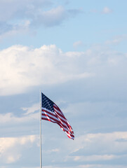 Vertical photo of American Flag against gray and white cumulus clouds and blue sky. The flag is unfurled in the breeze.