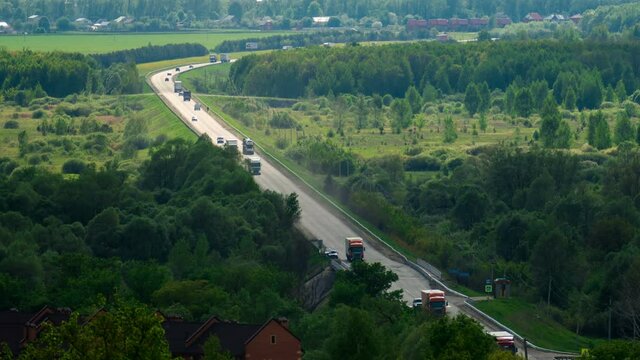 A large number of trucks and cars driving on a long road among the woods and fields. Timelapse
