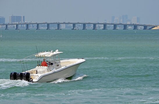 Sport fishing boat powered by three outboard engines cruising on the florida inter-coastal waterway with a Julia Tuttle Causeway bridge connecting Miami with Miami Beach in the background.