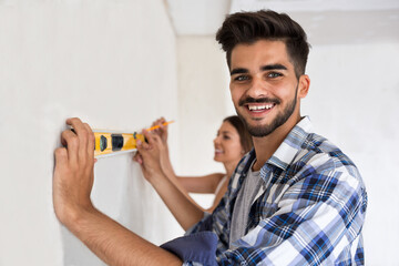 Smiling young couple measuring wall with level tool, renovation concept