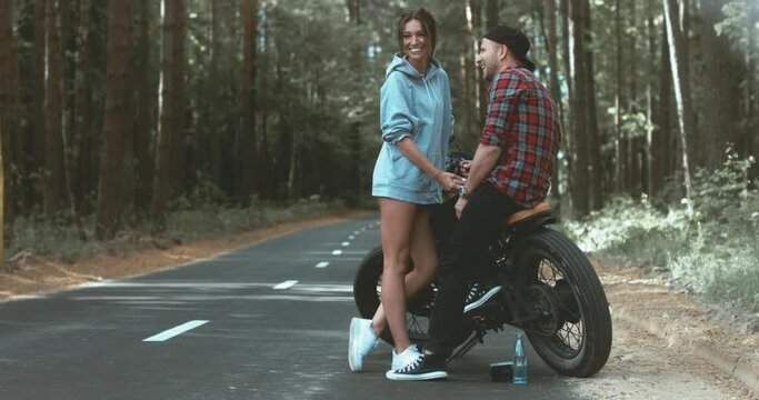 Young Caucasian couple on a motorcycle on the forest road. Love, freedom, togetherness concept. Couple travel on a motorbike. 4K UHD RAW edited footage 
