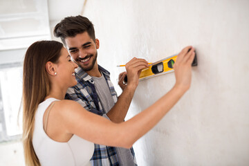 Smiling young couple measuring wall with level tool, renovation concept - obrazy, fototapety, plakaty