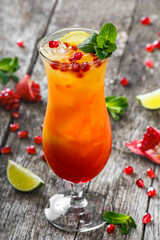 Fresh fruit tropic cocktail with mint, orange and pomegranate in tall glass on wooden background. Summer drinks and cocktails