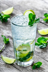 Fresh lemonade mojito with mint, lime and ice in glass on wooden background. Summer drinks and alcoholic cocktails