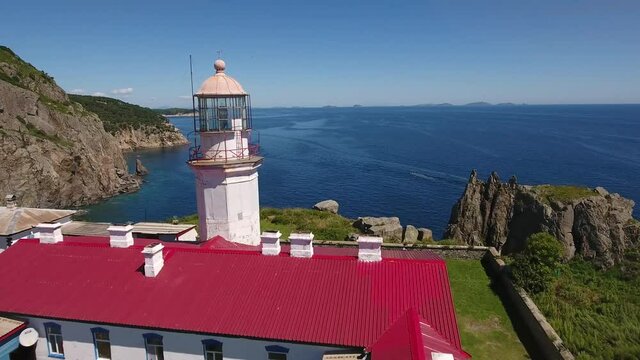 Famous Lighthouse Gamov peninsula forward close flight. Far East Marine Reserve, Primorsky Krai, Vladivostok, Russia. Unique National park Japan Sea. Aerial Helicopter Drone. Colorful summer day